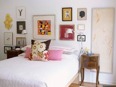 a white bed topped with lots of pillows next to pictures on the wall above it