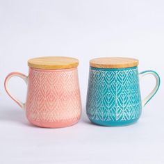 two ceramic mugs with wooden lids and designs on the sides, one blue and one pink