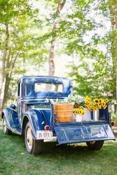 an old blue truck with sunflowers and flowers in the back is parked on grass