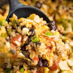 a spoon full of mexican rice with beans and corn on it is being lifted from the casserole dish