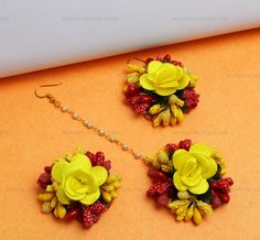 three pieces of jewelry with yellow flowers on them sitting on an orange surface next to pearls and beads