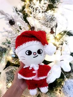 a hand holding a small stuffed animal in front of a christmas tree