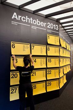 a woman standing next to a wall covered in yellow numbered signs with numbers on them