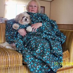 a woman sitting on a couch with her dog wrapped up in a blue and green blanket