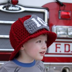 a young boy wearing a red hat standing in front of a fire truck