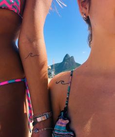 two women in bikinis standing next to each other with tattoos on their arms and shoulders