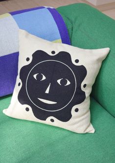 a pillow with a face drawn on it sitting on a green couch next to pillows