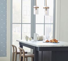 a kitchen island with two chairs and a table in front of large windows that have blue wallpaper on them