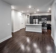 an empty kitchen and living room in a new home with wood flooring, stainless steel appliances and white walls