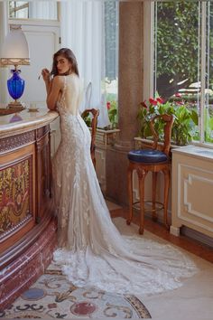 a woman in a wedding dress leaning on a counter with her back to the camera