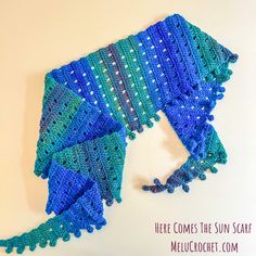 there is a blue and green crocheted shawl on the table with text overlay that says here comes the sun scarf