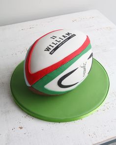 a rugby ball cake sitting on top of a green and white platter with the name milli written on it