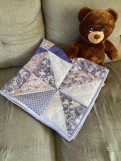 a brown teddy bear sitting on top of a couch next to a quilt