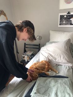 a woman petting an orange cat on top of a bed in a room with white walls