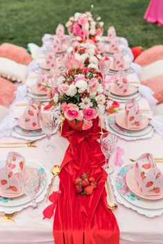 the table is set with pink and white plates, cups, and flowers on it