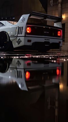 a white sports car parked in front of a building at night with its lights on