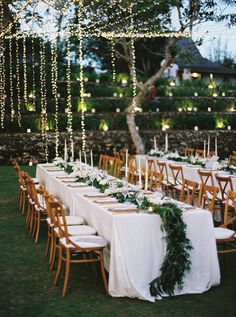 a long table with white linens and greenery is set up for an outdoor dinner