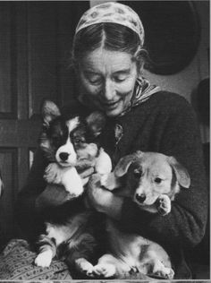 a woman holding four puppies in her arms while sitting on the floor next to another dog