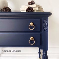 a blue dresser with pine cones and books on it's top, in front of a white wall