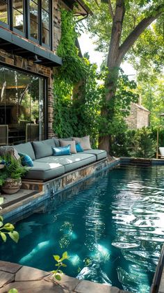 an outdoor living area next to a swimming pool with couches and trees in the background