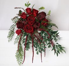 a bouquet of red roses and greenery on a white surface