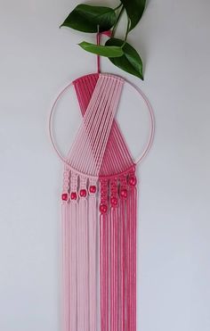 a pink wall hanging with beads and a plant