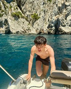 a man on a boat in the water near some rocks and cliffs with blue water