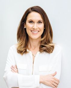 a woman standing with her arms crossed and looking at the camera, wearing a white shirt