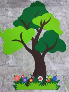 a paper cut out of a tree with flowers and grass on the ground next to it