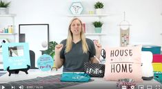 a woman sitting at a table holding up a pillow that says house and home on it