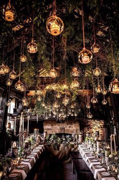 an indoor dining area with tables and lights hanging from the ceiling, surrounded by greenery