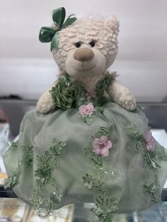 a teddy bear dressed in a green dress with flowers on it's chest and head