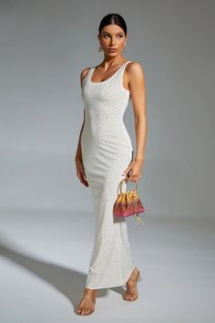 a woman in a white dress is holding a handbag and posing for the camera