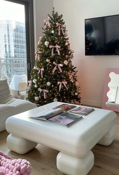 a living room with a christmas tree in the corner and pink accessories on the coffee table