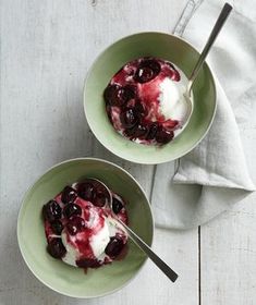 two bowls filled with ice cream and cherries on top of a white wooden table