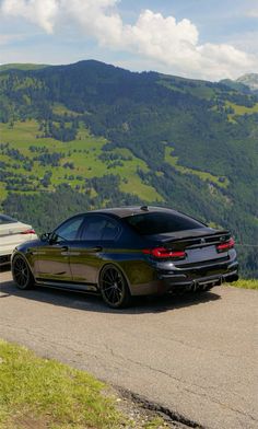 two cars parked on the side of a road in front of some hills and trees