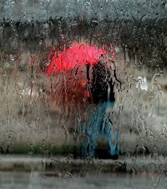 a person walking in the rain with an umbrella and holding a red umbrella over their head