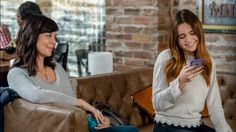 two women sitting on couches looking at their cell phones