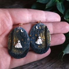 a pair of black and gold earrings with white ghost faces on them in front of a green plant