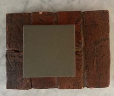 a square mirror sitting on top of a white counter next to a brick wall with cracks in it