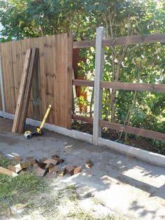 a wooden fence with pieces of wood in front of it and a tool laying on the ground