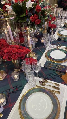 the table is set with plates, silverware and red roses