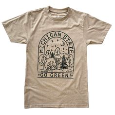 Sand colored t-shirt with green lettering spelling Michigan State arched over the top of a forest setting graphic, with Go Green across the bottom of the graphic. Eco-friendly Green Cotton T-shirt, Eco-friendly Short Sleeve T-shirt, Eco-friendly Cotton T-shirt For Earth Day, Eco-friendly Graphic Print T-shirt For Summer, Eco-friendly Graphic Print Top For Earth Day, Eco-friendly Organic Cotton Tops With Screen Print, Eco-friendly Cotton Top With Graphic Print, Eco-friendly Graphic Cotton T-shirt, Eco-friendly Graphic Tee In Cotton