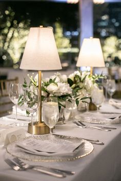 the table is set with silverware and white flowers in glass vases, along with two lamps