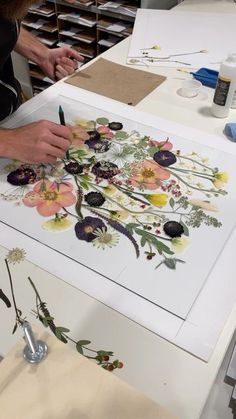 a woman is working on an art project with flowers and leaves painted on paper in front of her