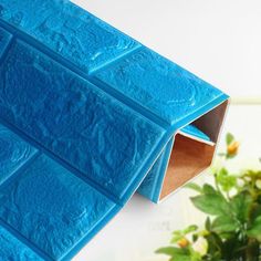 a blue vase filled with green plants next to a wall made out of plastic blocks