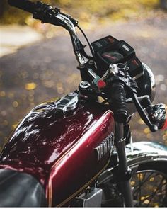 a red motorcycle parked on the side of a road next to a leaf covered forest