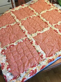 an orange and white quilt sitting on top of a wooden table next to a chair