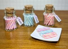 three glass jars filled with candy canes on top of a wooden table next to a plate