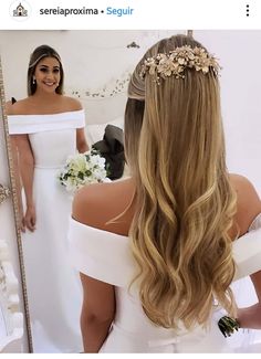 a woman in a white dress is looking at herself in the mirror with flowers on her head